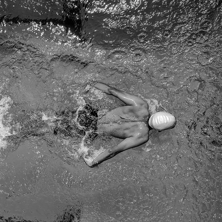 Man swimming freestyle in a pool captured from above with water splashing around him.
